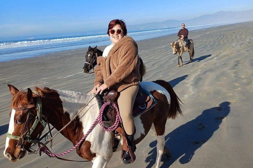 A person riding a horse on a beach with another horse and rider in the background. 2