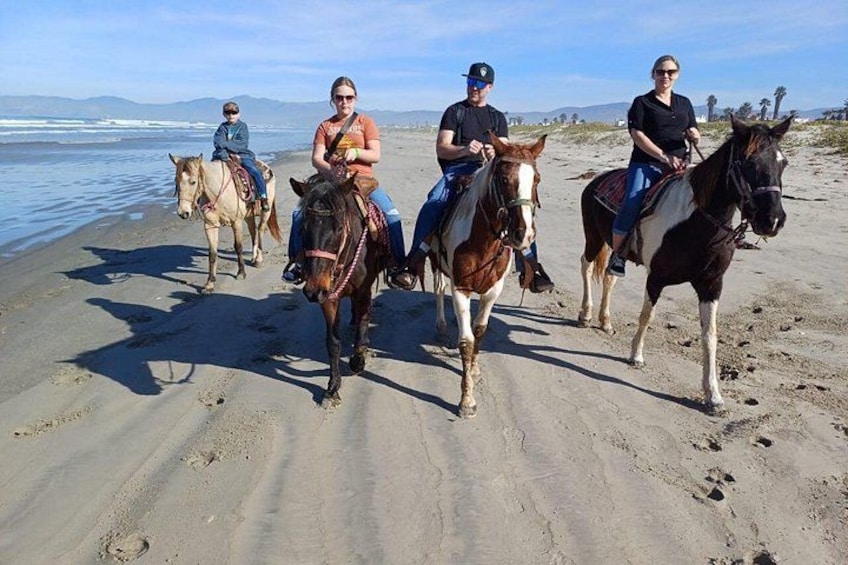 Four people riding horses on a sandy beach with the ocean in the background. 5