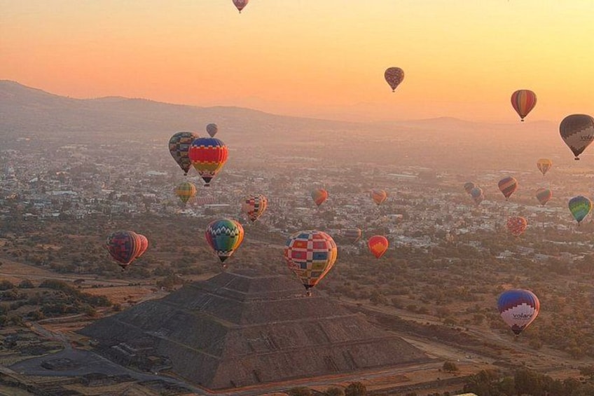 Paesaggio con diverse mongolfiere nel cielo e una struttura a forma di piramide a terra. 1