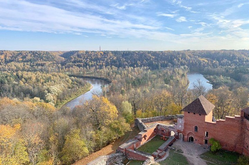 A historic brick building with a tower, surrounded by autumn foliage and a river. 1