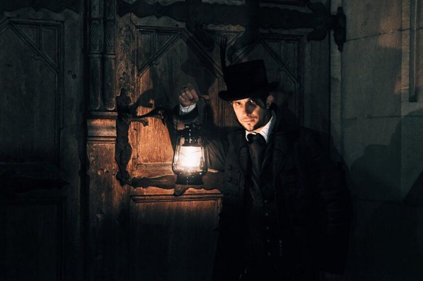 A person holding a lantern in a dimly lit room with wooden walls and a door. 2