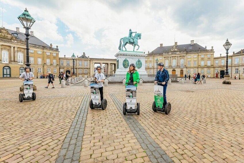 Three people riding Segways in a cobblestone square with historic buildings and a statue in the background. 5