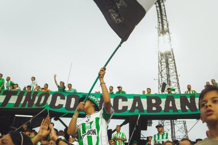 A crowd of people holding a banner with the text 'TITINOCABAN' and wearing green and white striped clothing. 3