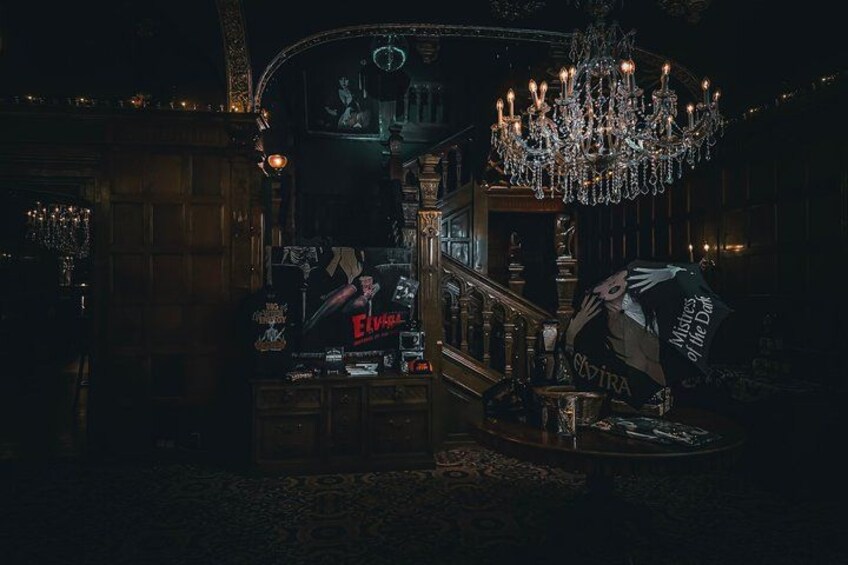 En svagt oplyst bar med en lysekrone, et skilt der siger 'Elvira', og en plakat af en kvinde med teksten 'MYSTERY of the Lark'. 2