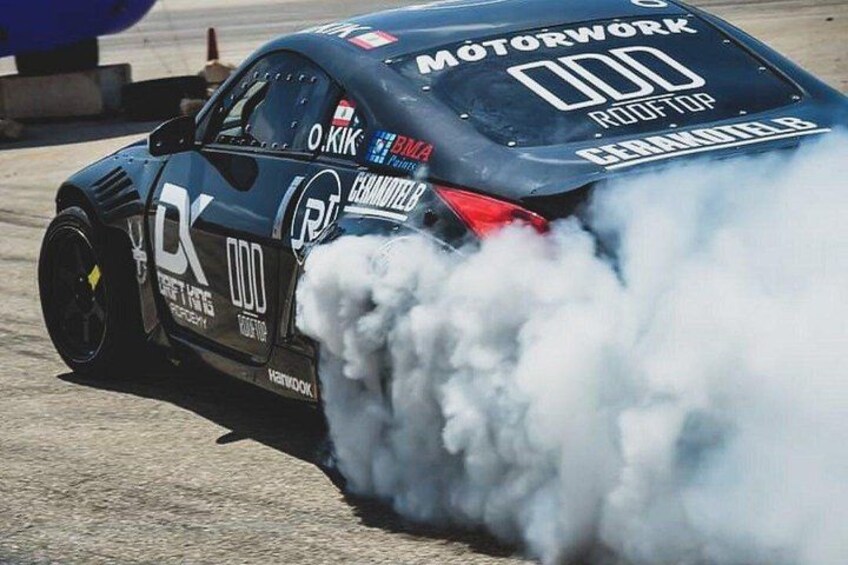 A car with smoke coming from its rear, a number '000' on the back, and various sponsor logos. 1