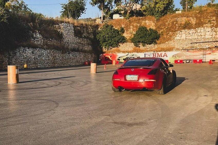 A red sports car parked in a parking lot with a stone wall and a banner in the background. 3