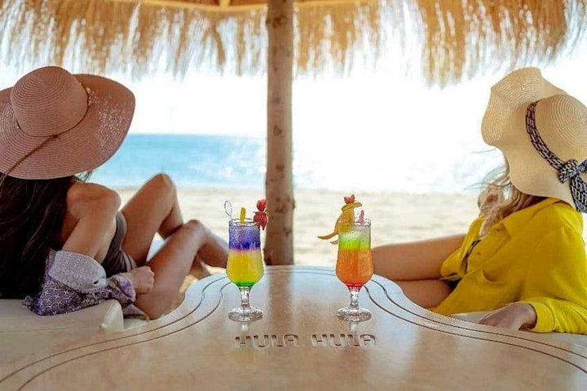 Two people sitting at a table with drinks on a beach. 3