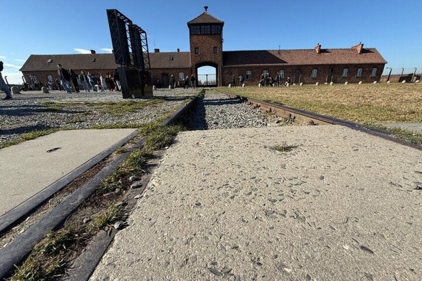 A historical building with a tower, a railway track, and a gravel area. 3