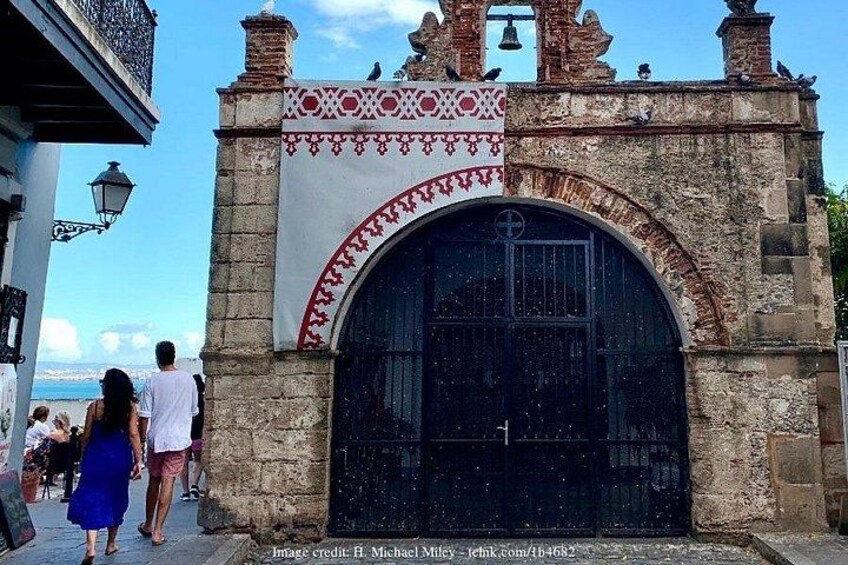 En historisk port av sten med en stor, välvd ingång, dekorativa mönster och en klocka ovanför. 3