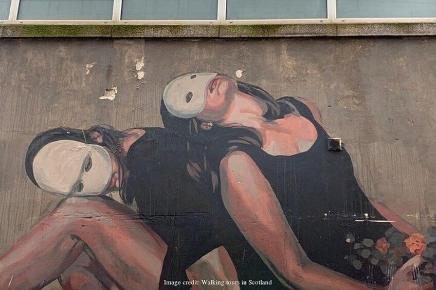 A mural of two figures with obscured faces, one in a black top and the other in a white top, on a concrete wall. 3