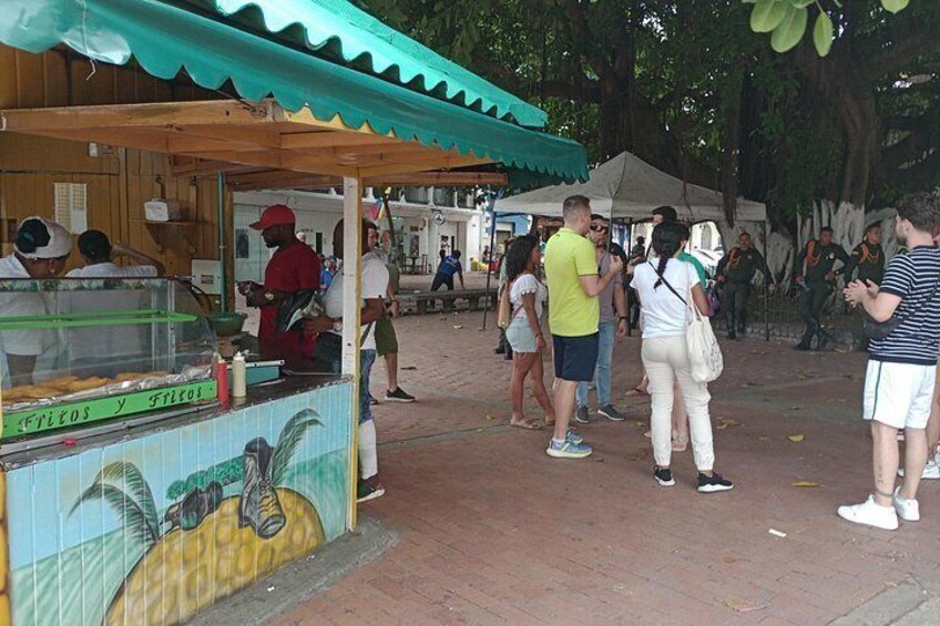 A food stall with a mural, people standing in line, and a shaded area. 3