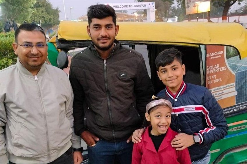 Four people standing in front of a green auto-rickshaw with advertisements on the side. 4