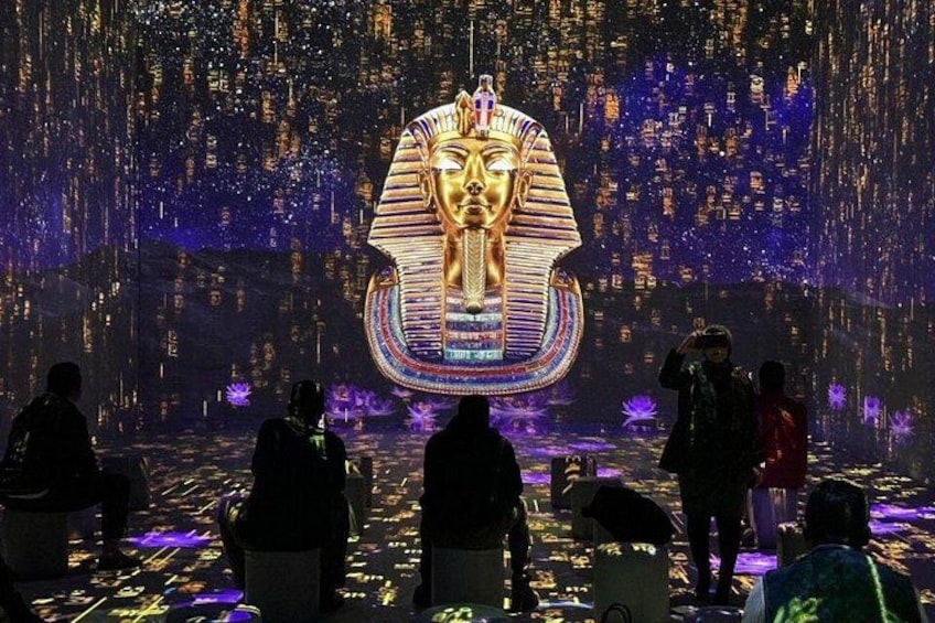 A large golden statue of a pharaoh's face with a headdress, surrounded by a crowd of people. 1
