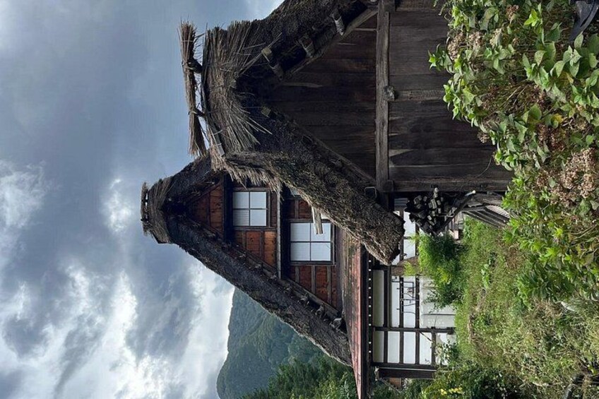 A rustic house with a thatched roof, surrounded by lush greenery and mountains in the background. 3