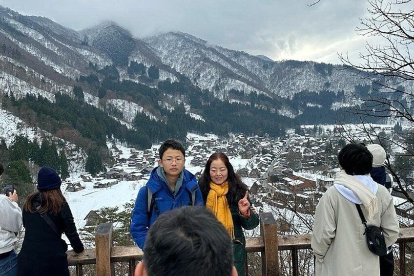 A group of people standing on a wooden platform overlooking a snow-covered valley with mountains in the background. 3