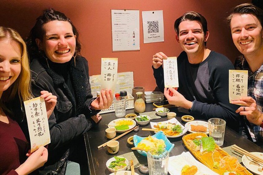 A group of people sitting around a table with various dishes and chopsticks, holding menus with Japanese characters. 3