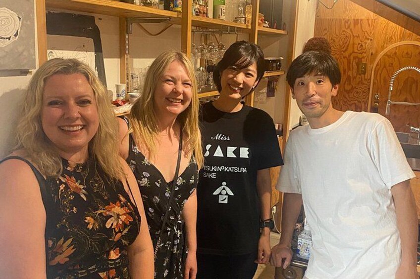 Four people standing indoors with shelves in the background. 4