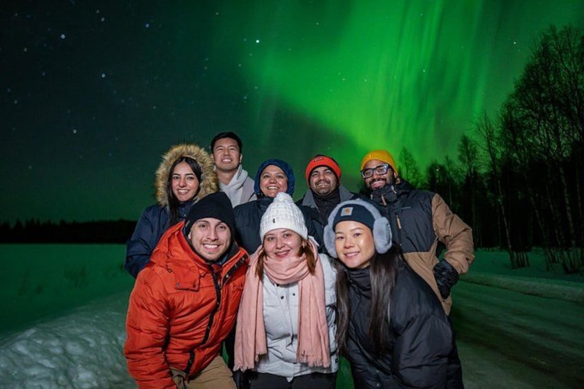 En gruppe mennesker ude om natten med grøn nordlys på himlen. 5