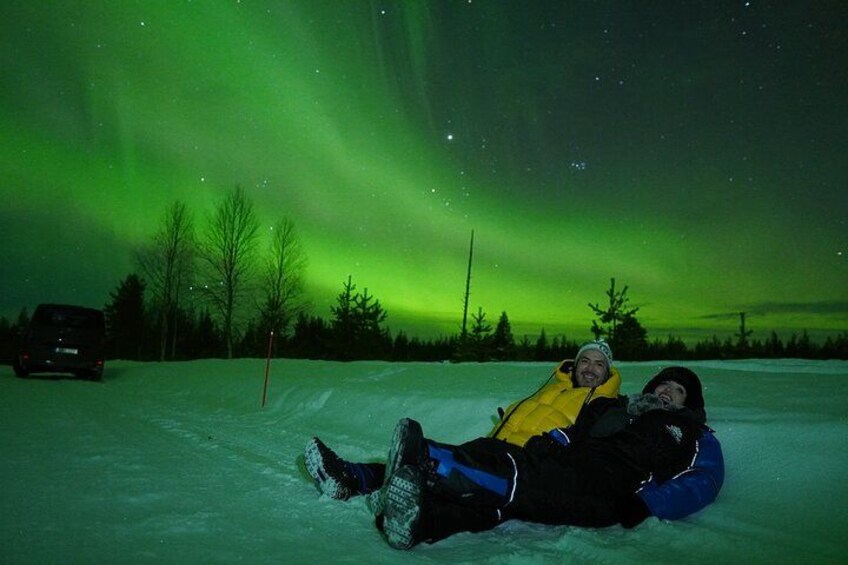 Deux personnes dévalent une pente enneigée sur une luge, sous une aurore boréale verte. 2