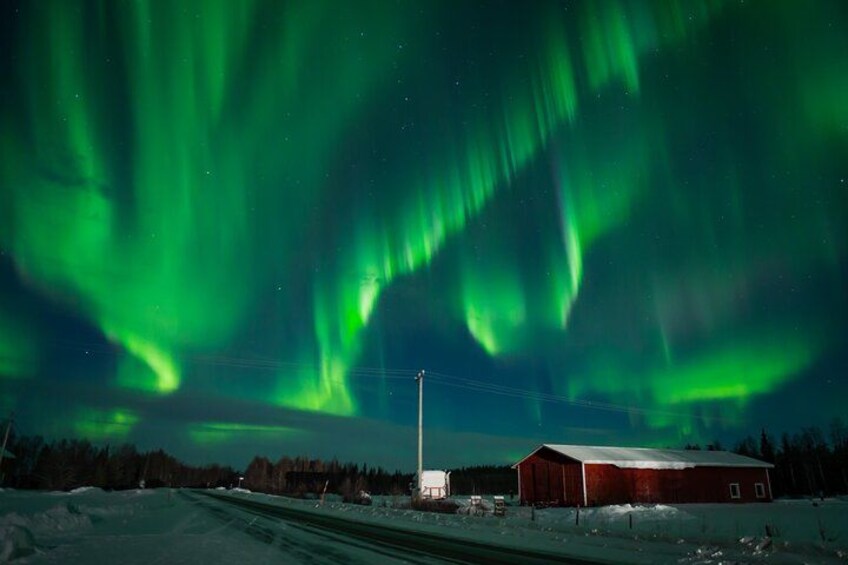 A snowy landscape with a red building and the aurora borealis in the sky. 2