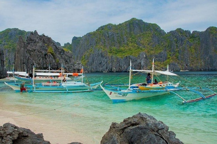 Une rangée de bateaux traditionnels est amarrée près d’une côte rocheuse, dans une eau turquoise et limpide. 4