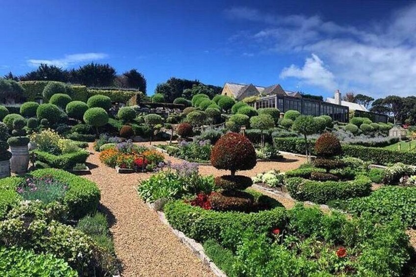 A well-manicured garden with a gravel path, neatly trimmed hedges, and a variety of colorful flowers. 1