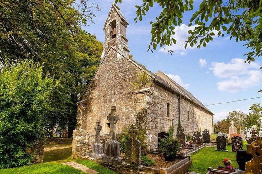 Een stenen kerk met een klokkentoren, omringd door een begraafplaats met grafstenen. 2