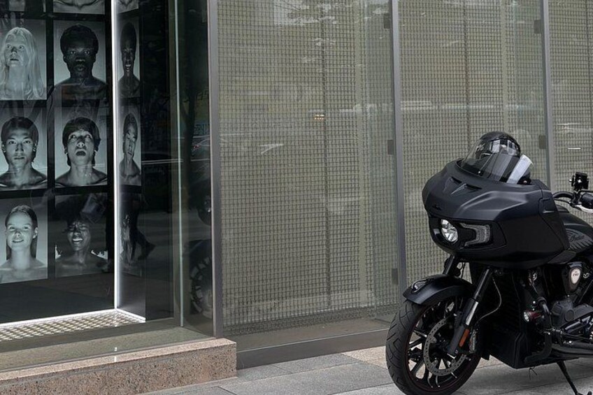Een zwarte motorfiets geparkeerd voor een gebouw met glazen ramen. 2