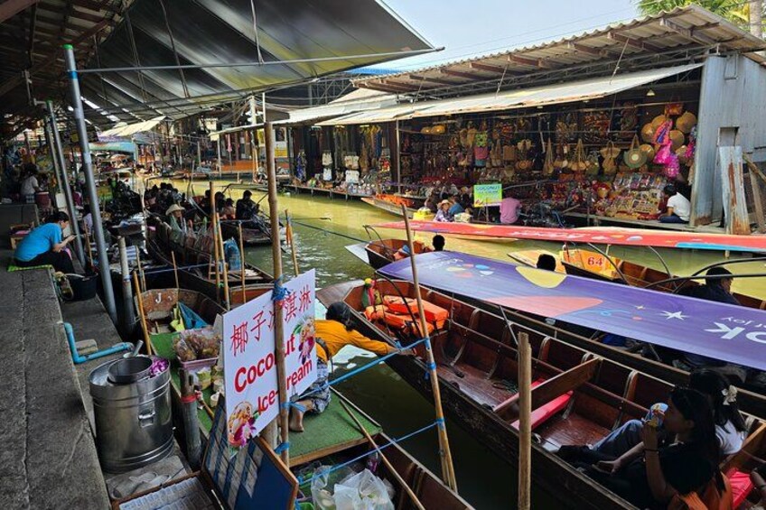 A floating market with boats docked, people shopping, and a sign for coconut ice cream. 5