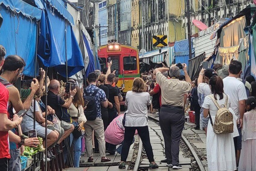 A crowded street with a train passing through, people taking photos, and a blue tarp-covered structure. 2