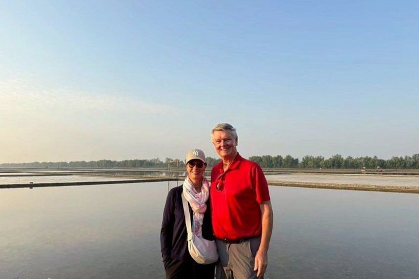Two people standing on a flat, expansive water body with a clear sky and distant trees. 3