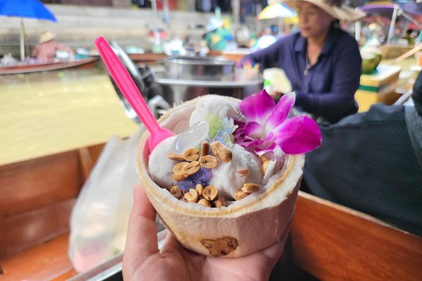 A hand holding a cup with a dessert, a pink spoon, and a purple flower. 5