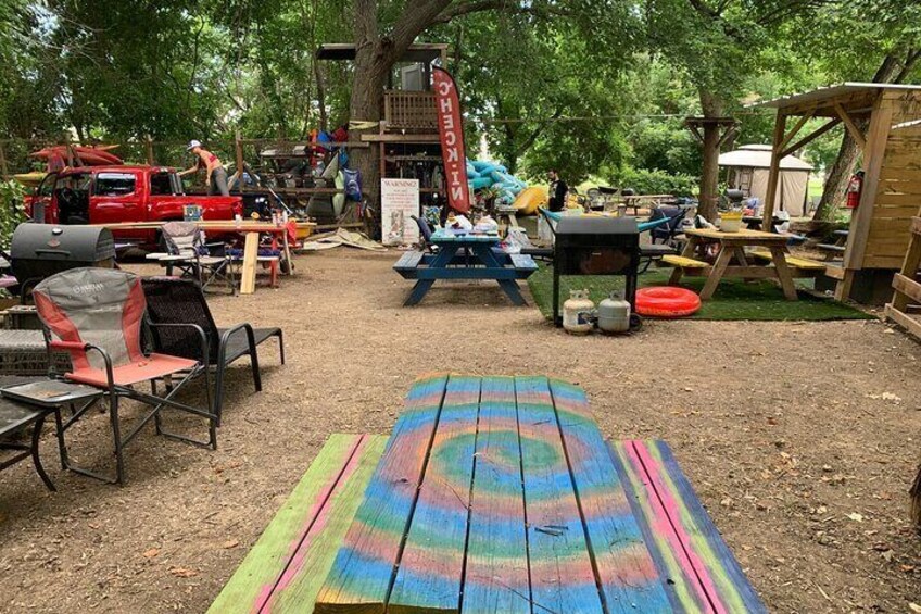 A colorful picnic area with a rainbow-striped blanket, picnic tables, and a red truck in the background. 1