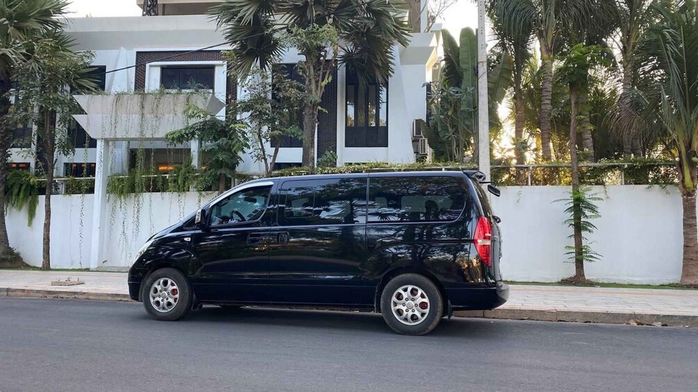 Ein schwarzer Minivan parkt auf einer Straße, im Hintergrund ein weißes Gebäude und Palmen. 5