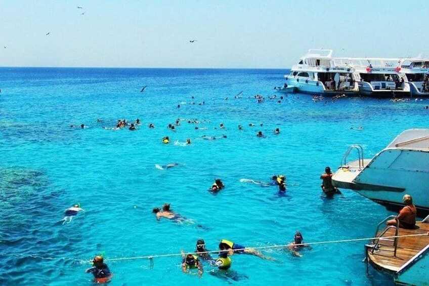 A group of people swimming in the ocean, a boat docked nearby, and a clear blue sky. 1