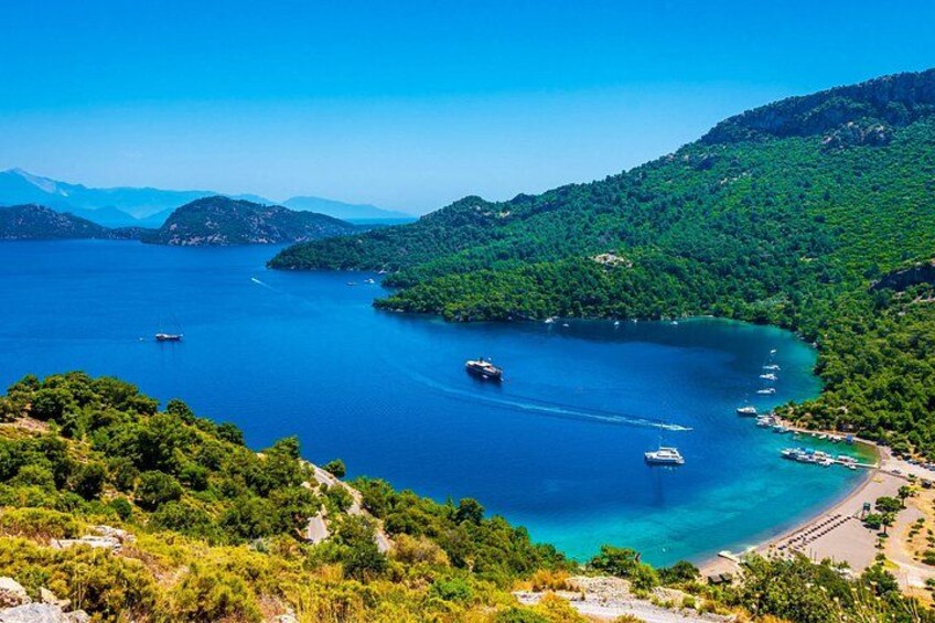 A coastal landscape with a clear blue sea, boats, and lush green hills. 3