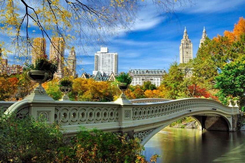A stone bridge over a river with autumn foliage and historic buildings in the background. 1