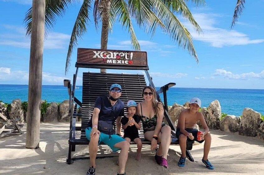 En familj på en strand, med en skylt som visar texten ”Xcaret, Mexiko”. 4
