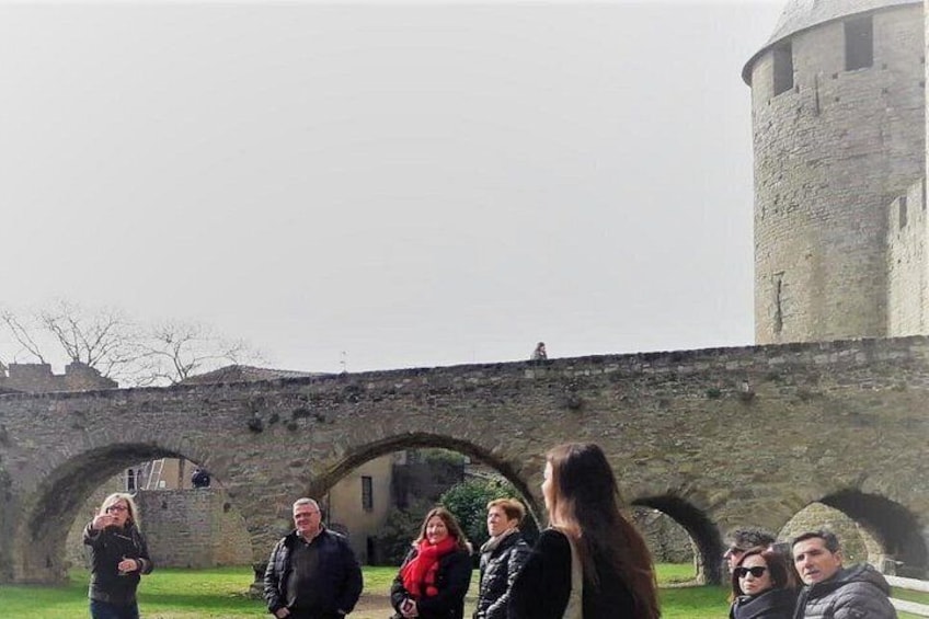 Een groep mensen staat voor een stenen brug met bogen en een ronde toren. 5