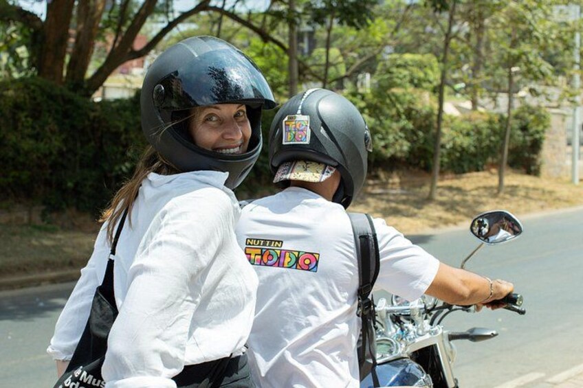 Two people on a motorcycle, one wearing a helmet and a white shirt with a graphic design. 4