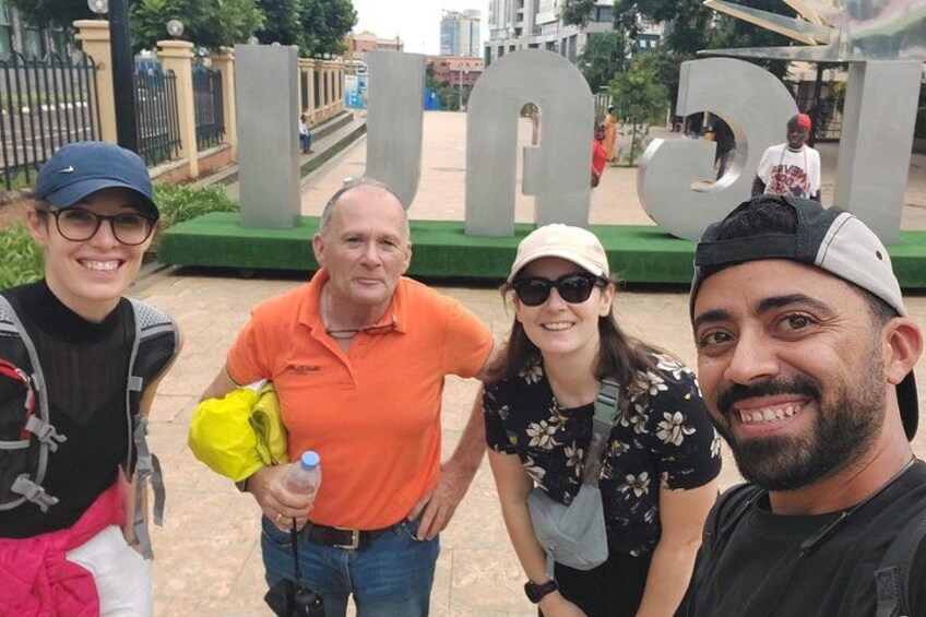 A group of people standing in front of a large, metallic sculpture with the letters 'U' and 'D' visible. 3