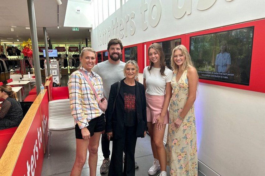 A group of people posing in front of a wall with a red and white design, a store interior with clothing racks, and a red carpeted area. 4