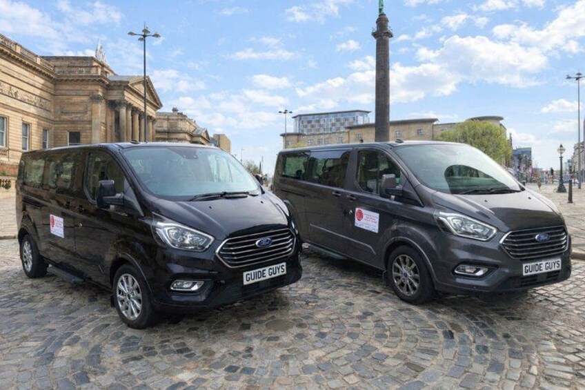 Two black vans parked on a cobblestone street with historic buildings in the background. 5