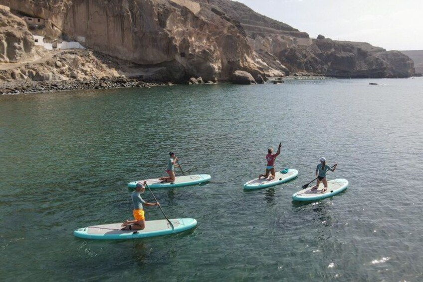 Des personnes pratiquent le paddle sur une étendue d’eau calme, avec des falaises en arrière-plan. 1
