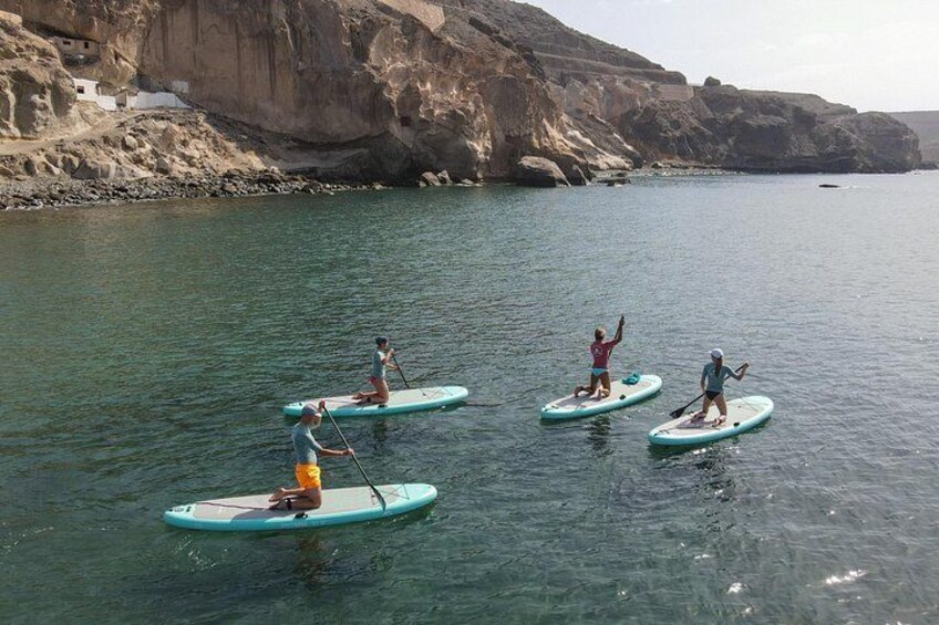 Folk padler på paddleboards på et roligt vandareal med klipper i baggrunden. 1