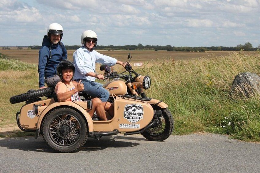 A person riding a sidecar motorcycle on a paved road with grass on the sides. 2