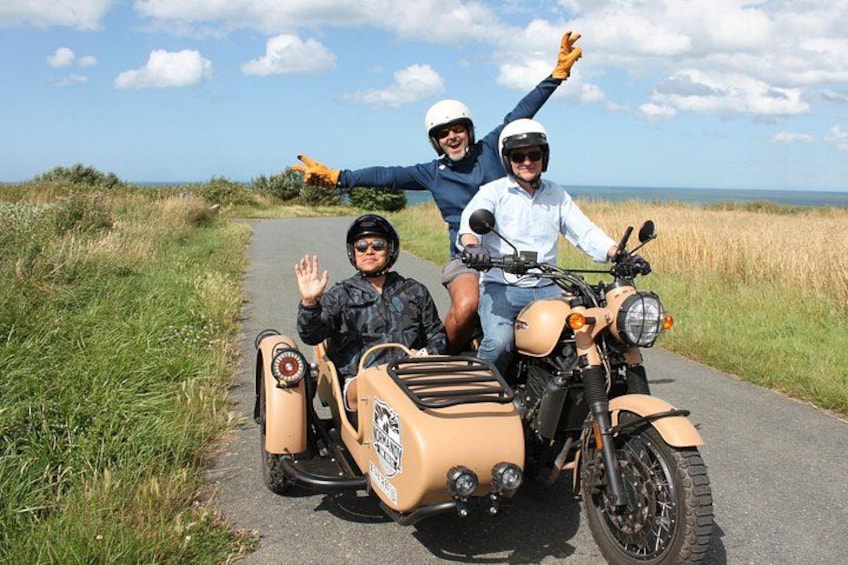 A motorcycle with a sidecar on a paved road with grass on the sides. 2