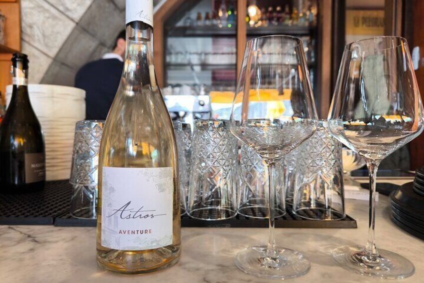 A bottle of wine labeled 'Aventure' and several empty wine glasses on a bar counter. 5
