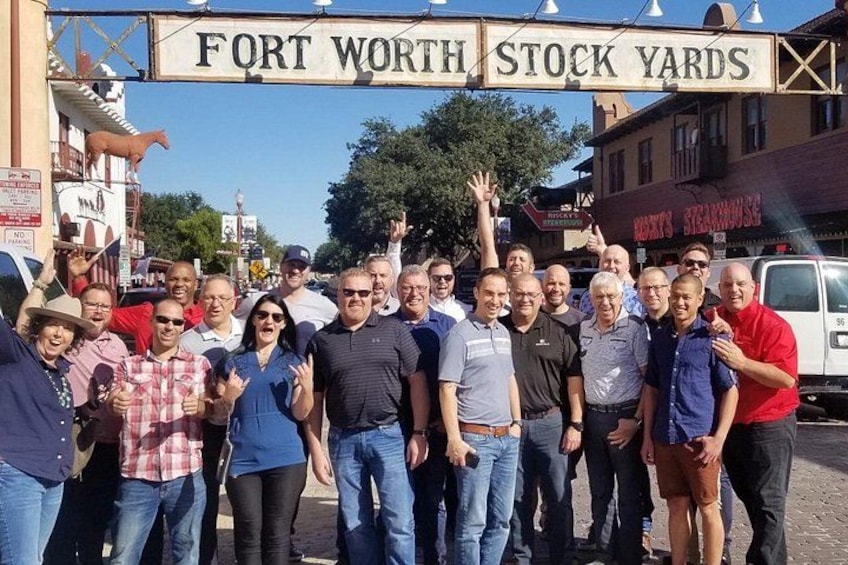 A group of people standing in front of a sign that reads 'FORT WORTH STOCK YARDS.' 2