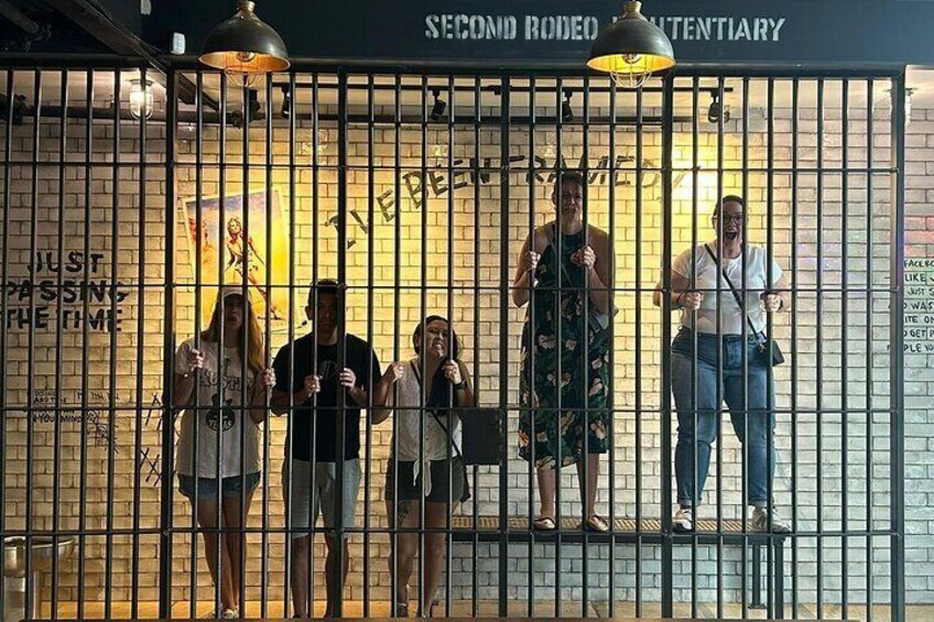 Eine Gruppe von Menschen steht hinter einem Metallzaun mit Graffiti und einem Schild, auf dem 'SECOND RODEO CANTON TENT' steht. 2